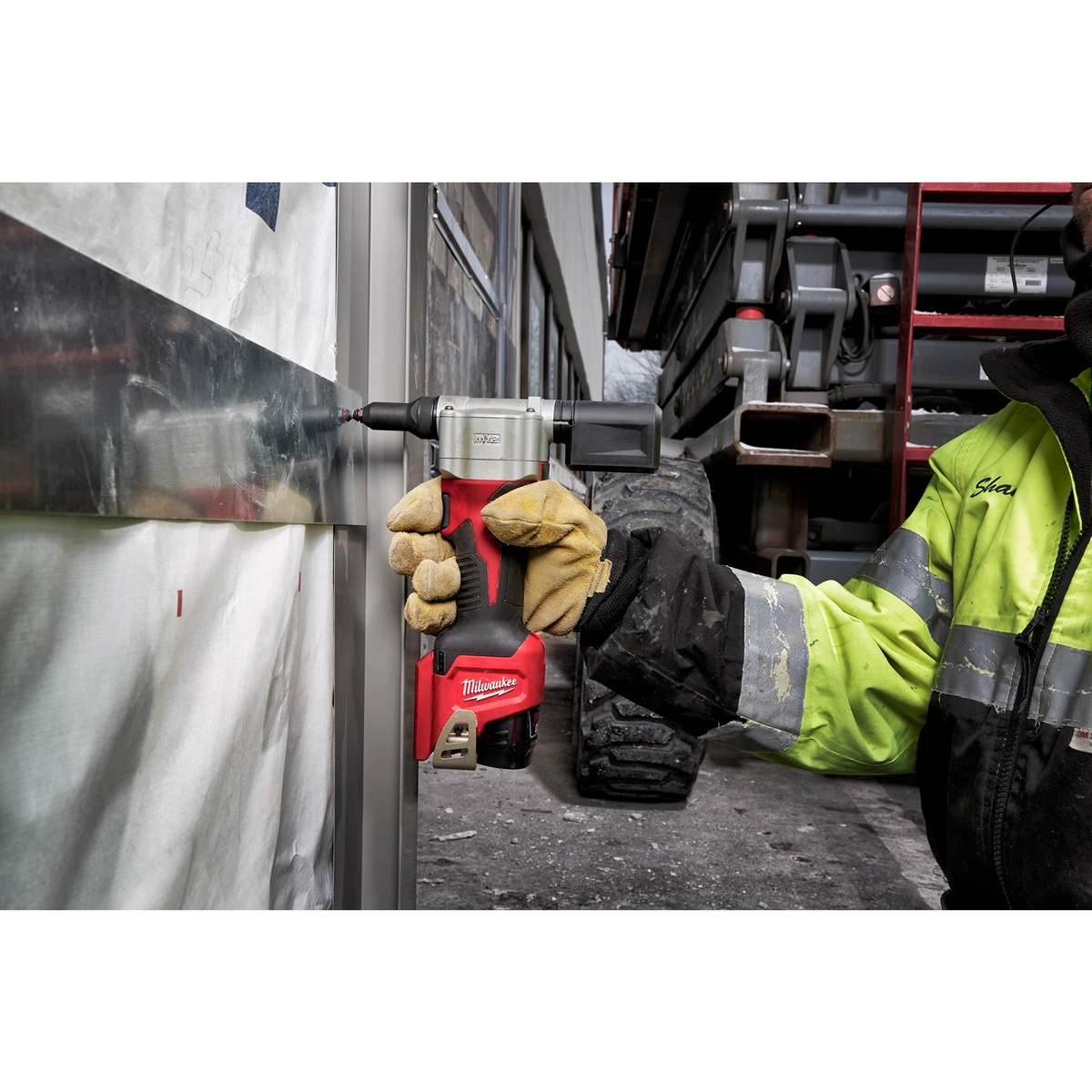 Milwaukee 2550-20 M12 Rivet Tool fastening a metal panel on a jobsite exterior wall with a worker wearing gloves