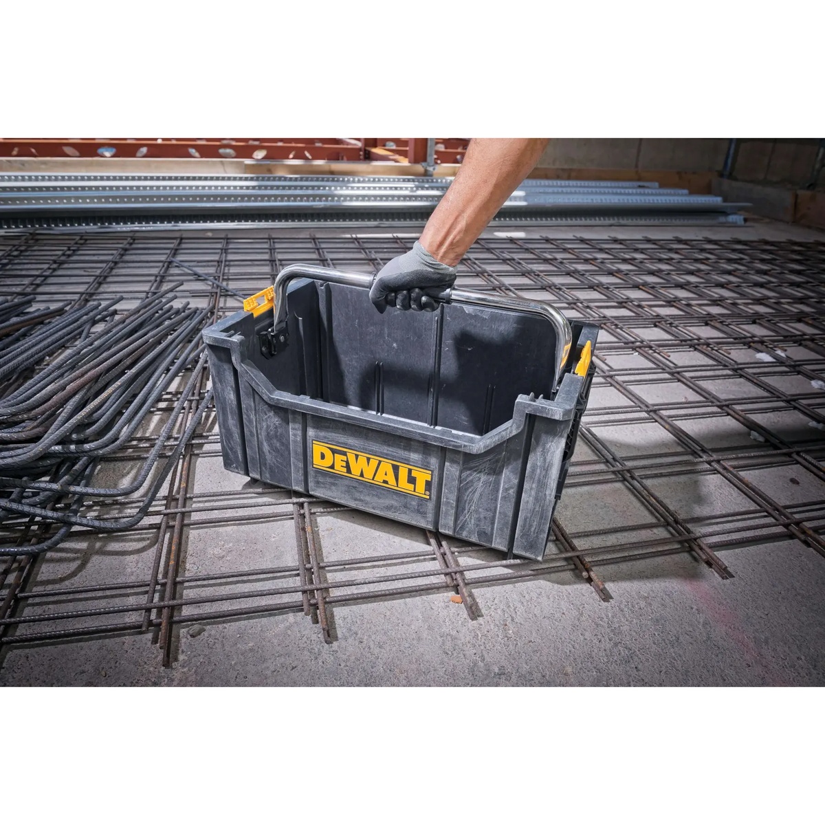 DEWALT ToughSystem Tote with Carrying Handle set down on a reinforced concrete jobsite floor showing open-top access and metal handle
