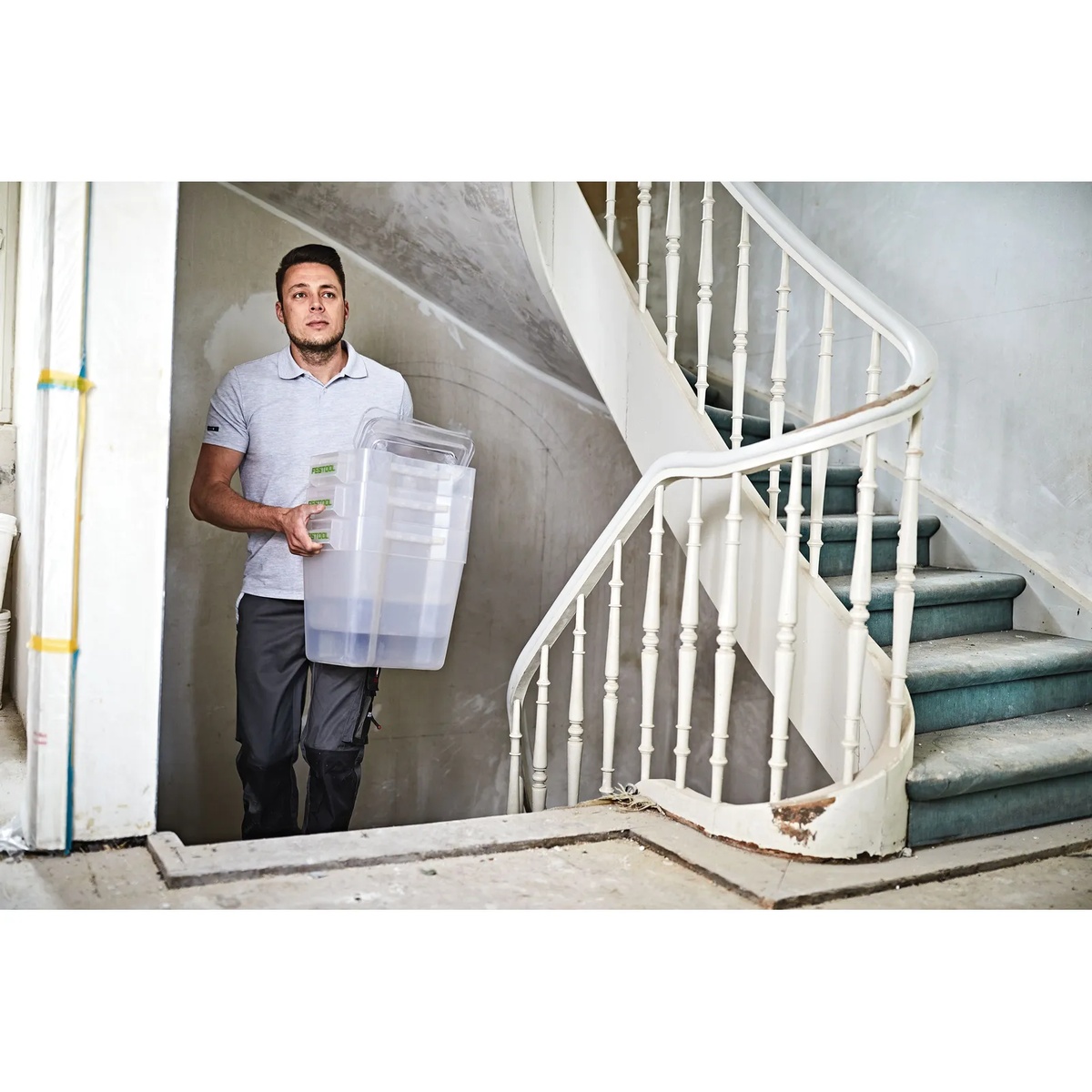 User carrying the clear collection container from the Festool CT Cyclone Dust Collection Pre-Separator CT-VA 20 through an interior renovation site for dust disposal