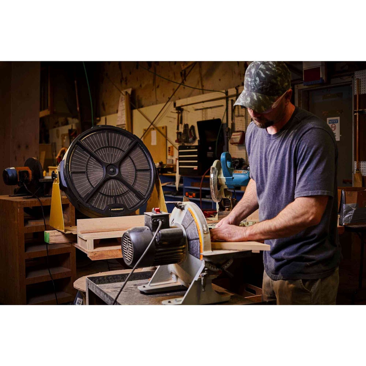 Powermatic 1791331 PM1250 Micro-Dust Air Filtration System running in a woodworking shop near a miter saw while cutting wood to reduce airborne dust during indoor shop work