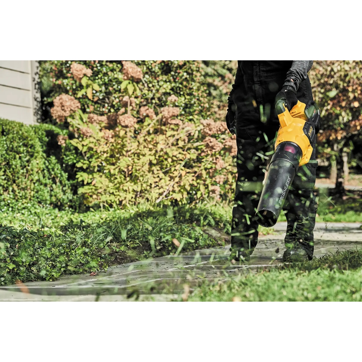 DEWALT DCBL772X1 FLEXVOLT 60V MAX brushless cordless handheld axial blower clearing grass clippings and debris from a sidewalk in a residential yard during outdoor cleanup