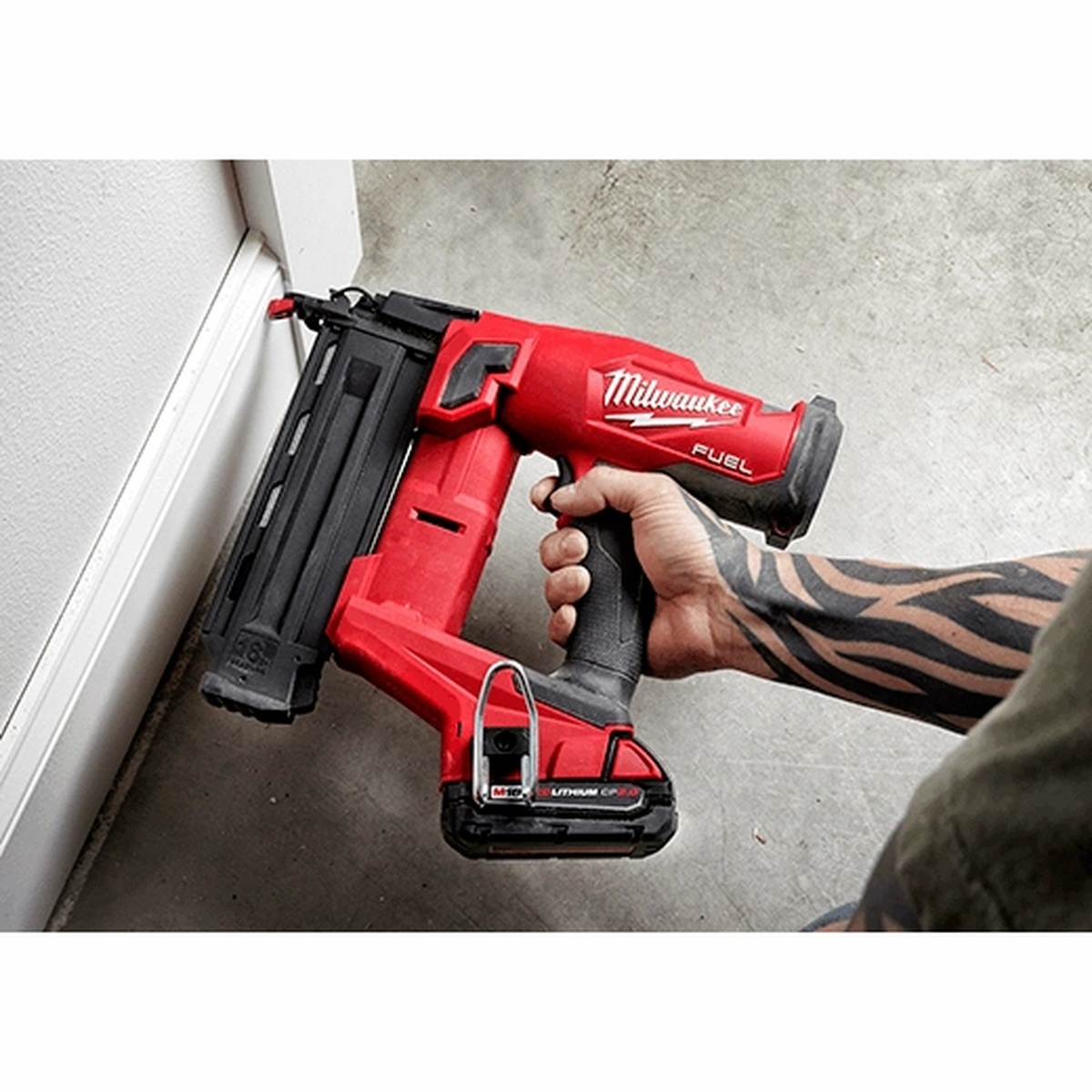 Milwaukee M18 FUEL 18 Gauge Brad Nailer driving a brad into interior trim near a wall and floor in a finished room