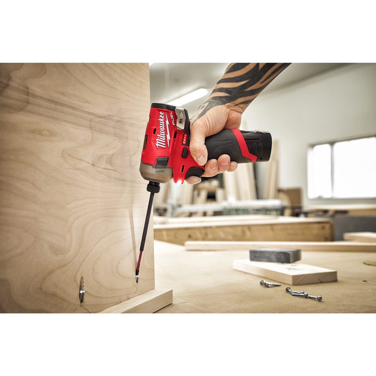 Milwaukee M12 FUEL SURGE 1/4 in. Hex Hydraulic Driver driving a screw into plywood in a workshop setting during cabinet or woodworking assembly