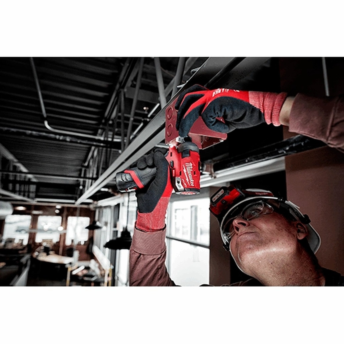 Milwaukee M12 FUEL SURGE 1/4 inch Hex Hydraulic Driver Kit driving fasteners overhead into steel framing in an indoor jobsite setting