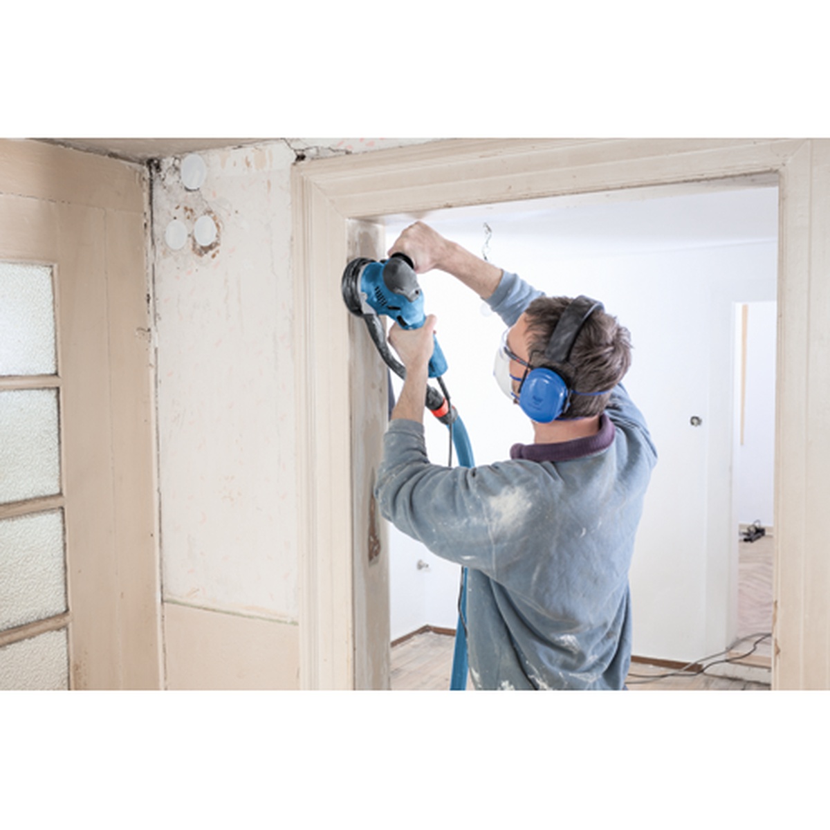 Bosch GET65-5N 5 In. Dual-Mode Random Orbit Sander sanding interior wood trim around a doorway during remodeling work