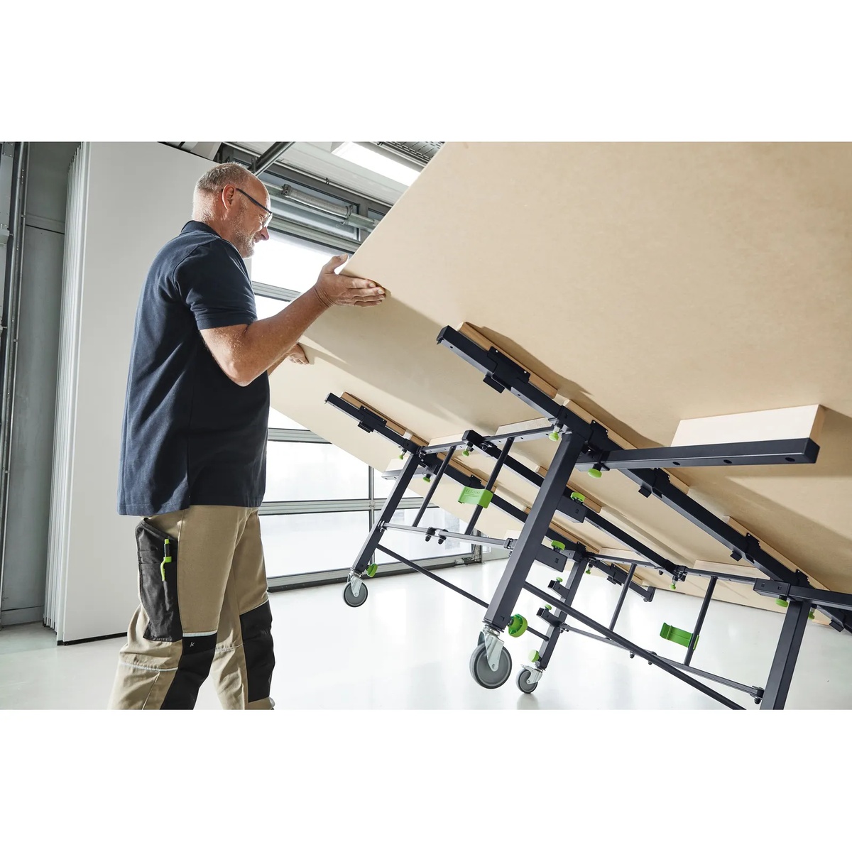 Festool 205183 STM 1800 Mobile Sawing Table supporting a large sheet panel in a shop while one user loads the material using the tilting function