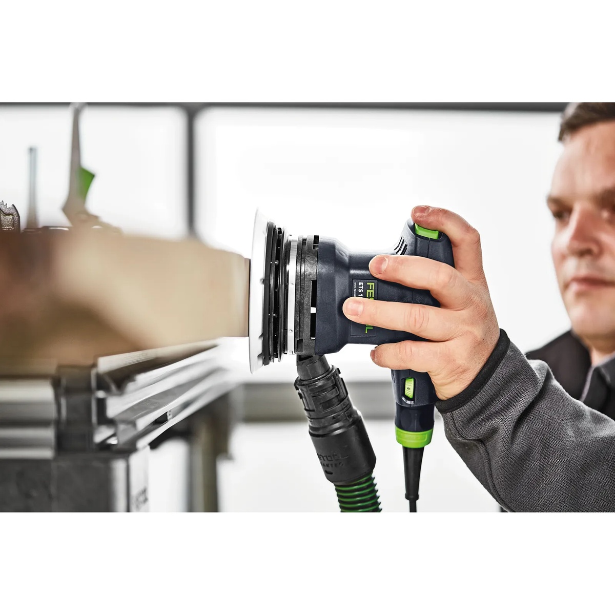 Festool 576070 ETS 125 REQ-Plus 125mm (5 inch) Random Orbital Sander sanding a vertical wood edge with dust extraction attached in a workshop setting