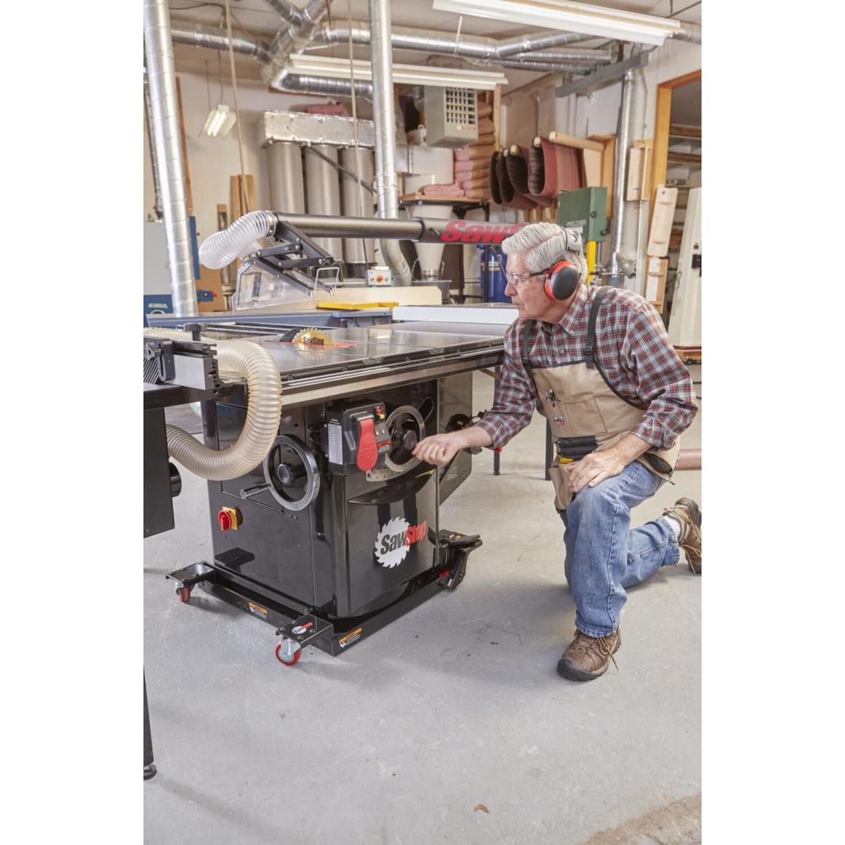 Woodworker adjusting blade height and bevel controls on a SawStop industrial cabinet saw in a production woodworking environment