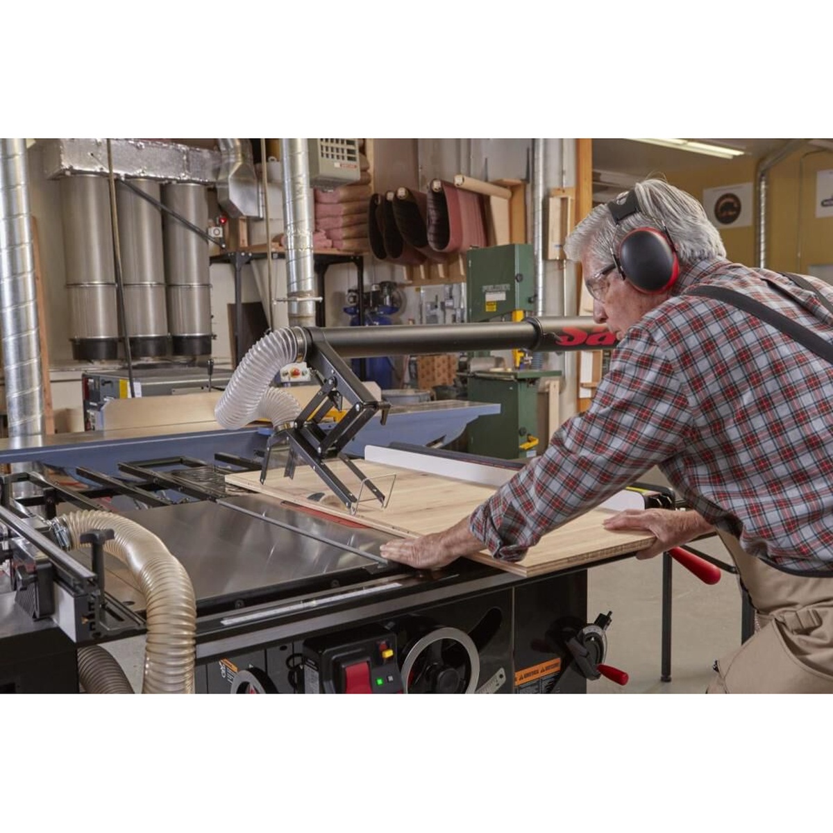 Industrial cabinet saw cutting plywood with overhead dust collection blade guard connected in a woodworking shop