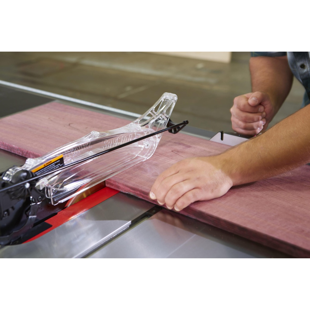 SawStop PCS31230-TGP236 Professional Cabinet Saw cutting a hardwood board under the dust collection blade guard during rip cutting in a workshop
