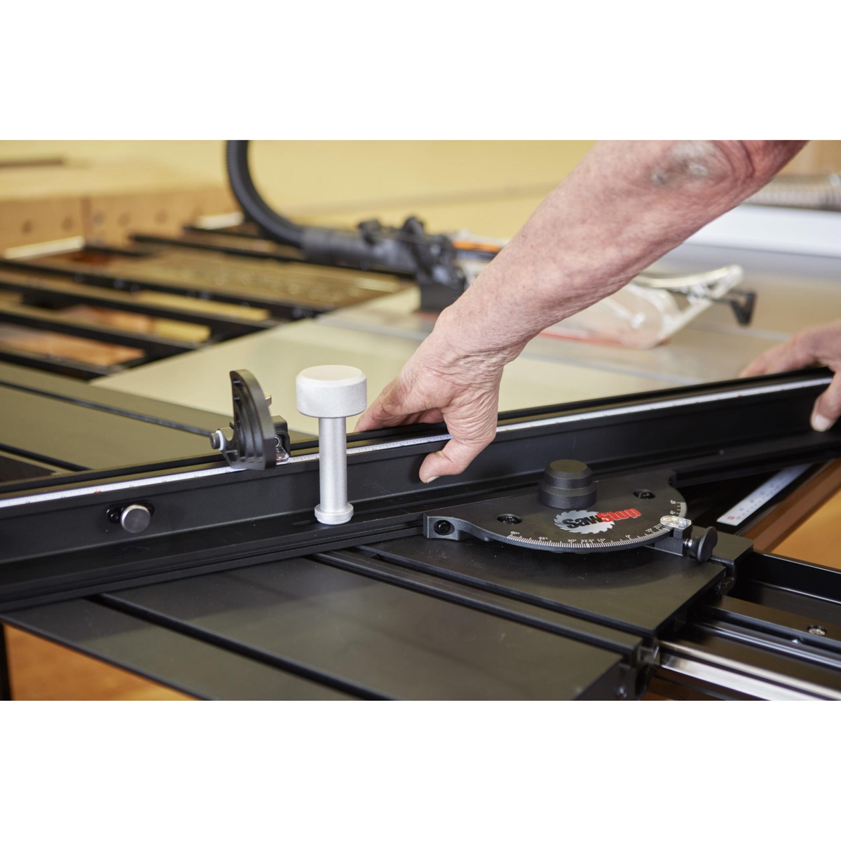 Close-up of the SawStop Sliding Crosscut Table handle, angle scale, and sliding table assembly on a SawStop saw in a workshop