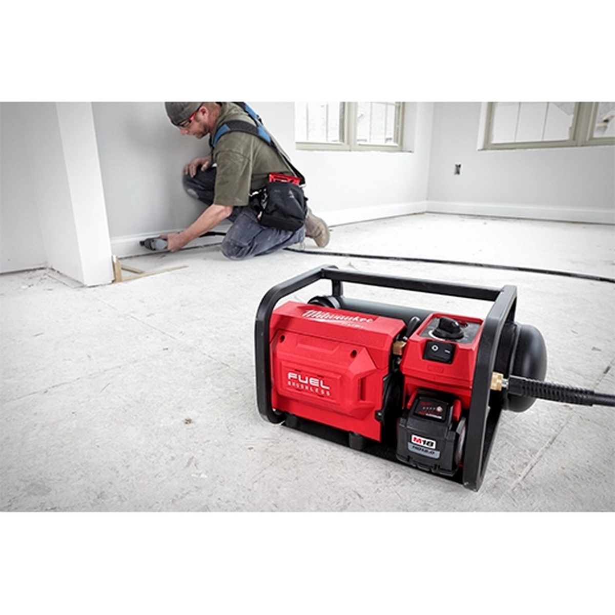 Milwaukee 2840-20 M18 FUEL 2 Gallon Compact Quiet Compressor powering interior trim work on a remodel jobsite floor with hose attached