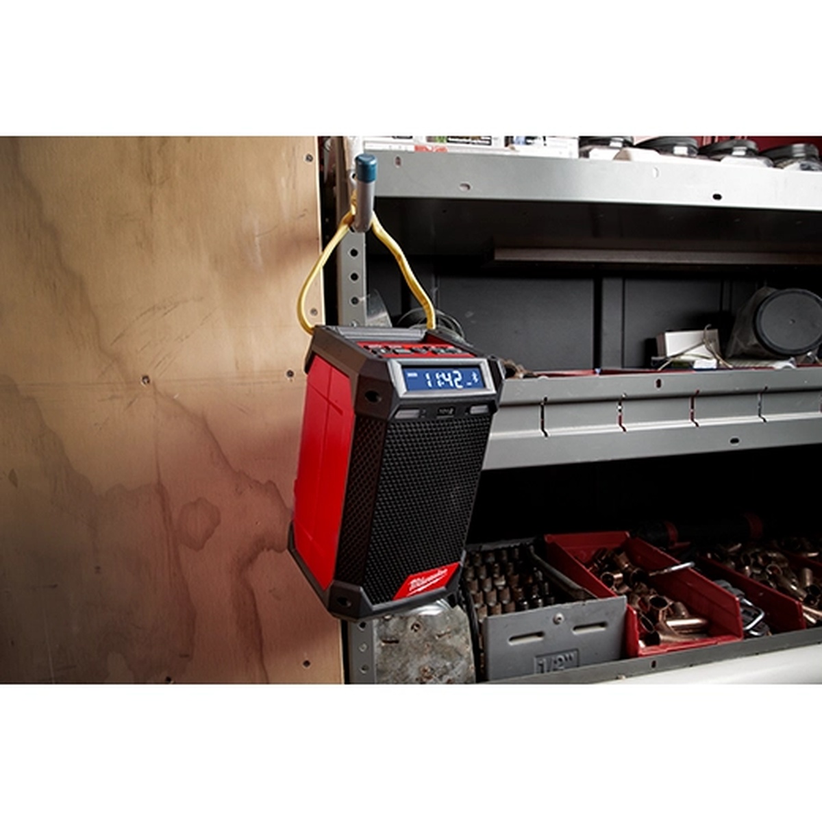 Milwaukee 2951-20 M12 Radio + Charger hanging on shelving in a workshop with tools and hardware nearby for off-the-bench jobsite audio