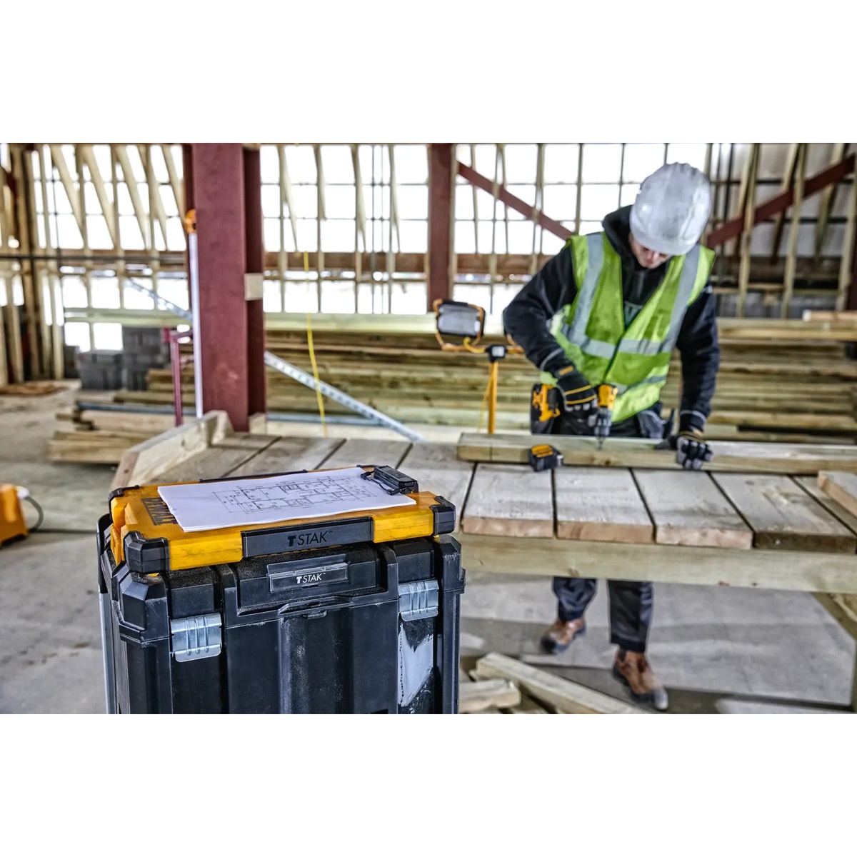 DEWALT DWST17818 TSTAK Mobile Storage Clipboard mounted on a TSTAK box holding jobsite plans on a construction table during active wood framing work