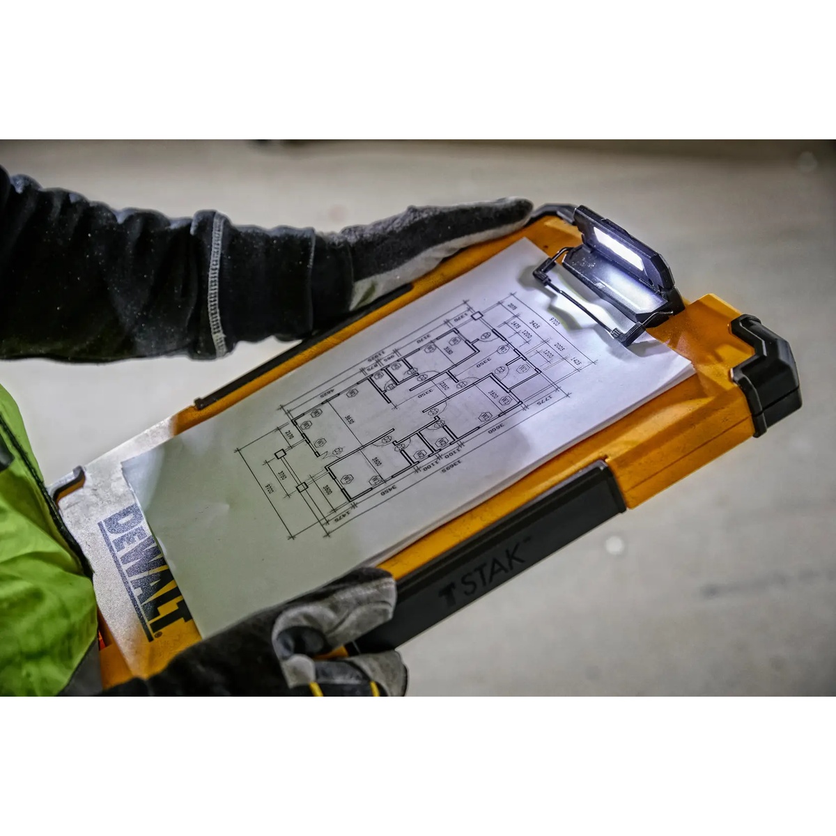 DEWALT DWST17818 TSTAK Mobile Storage Clipboard illuminating a printed floor plan with the integrated LED work light in a dim indoor jobsite setting