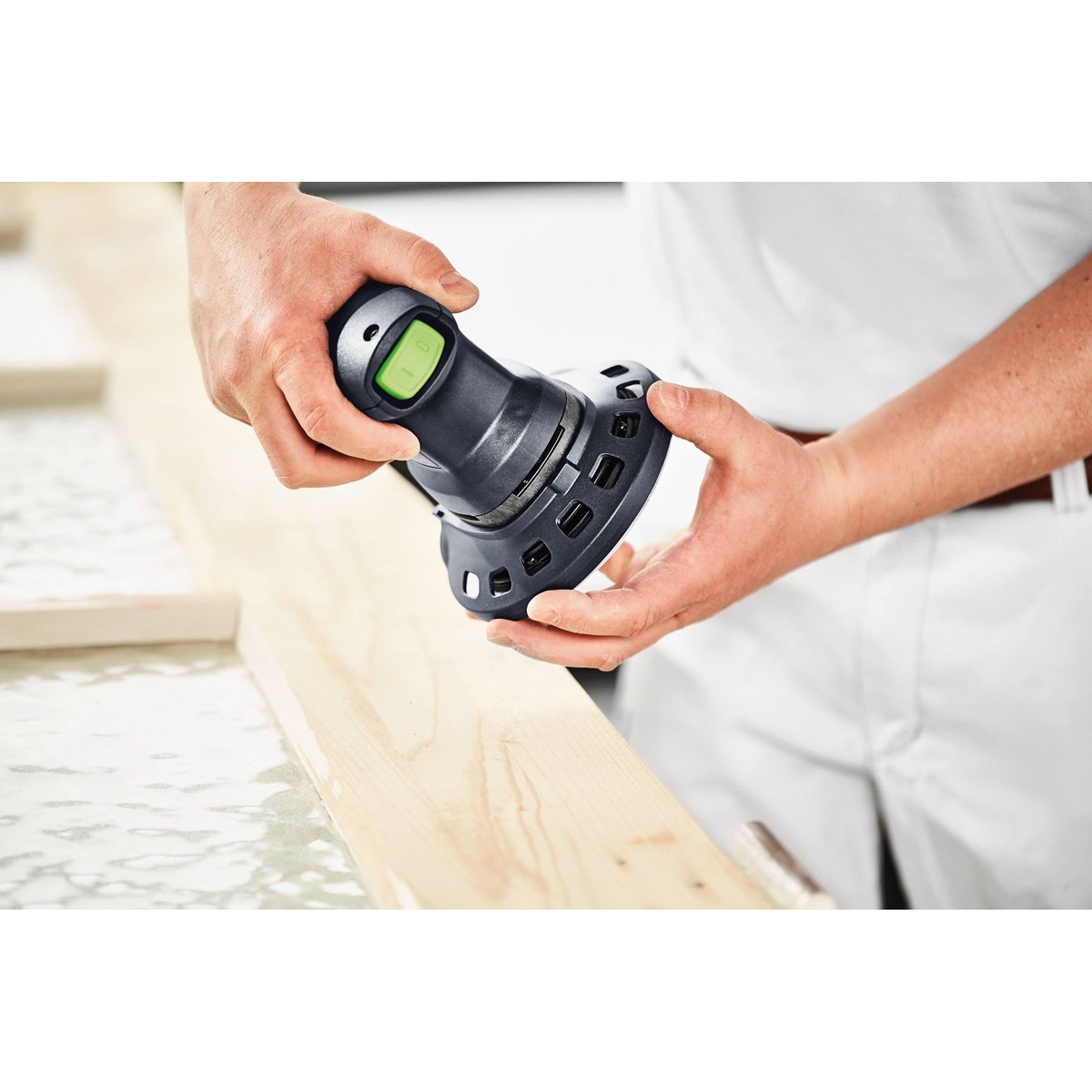 Festool ETS 125 REQ-Plus 125mm random orbital sander showing ergonomic one-handed grip and vented body during setup over a wood board