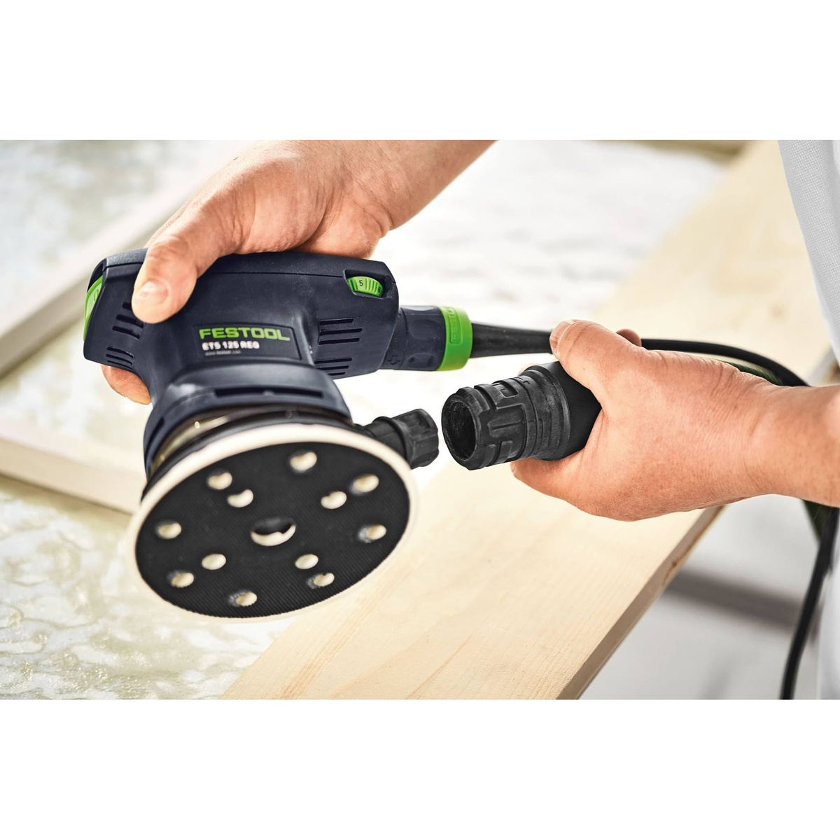 Festool ETS 125 REQ-Plus 125mm random orbital sander with bayonet dust extraction port being connected to a hose over a wood work surface