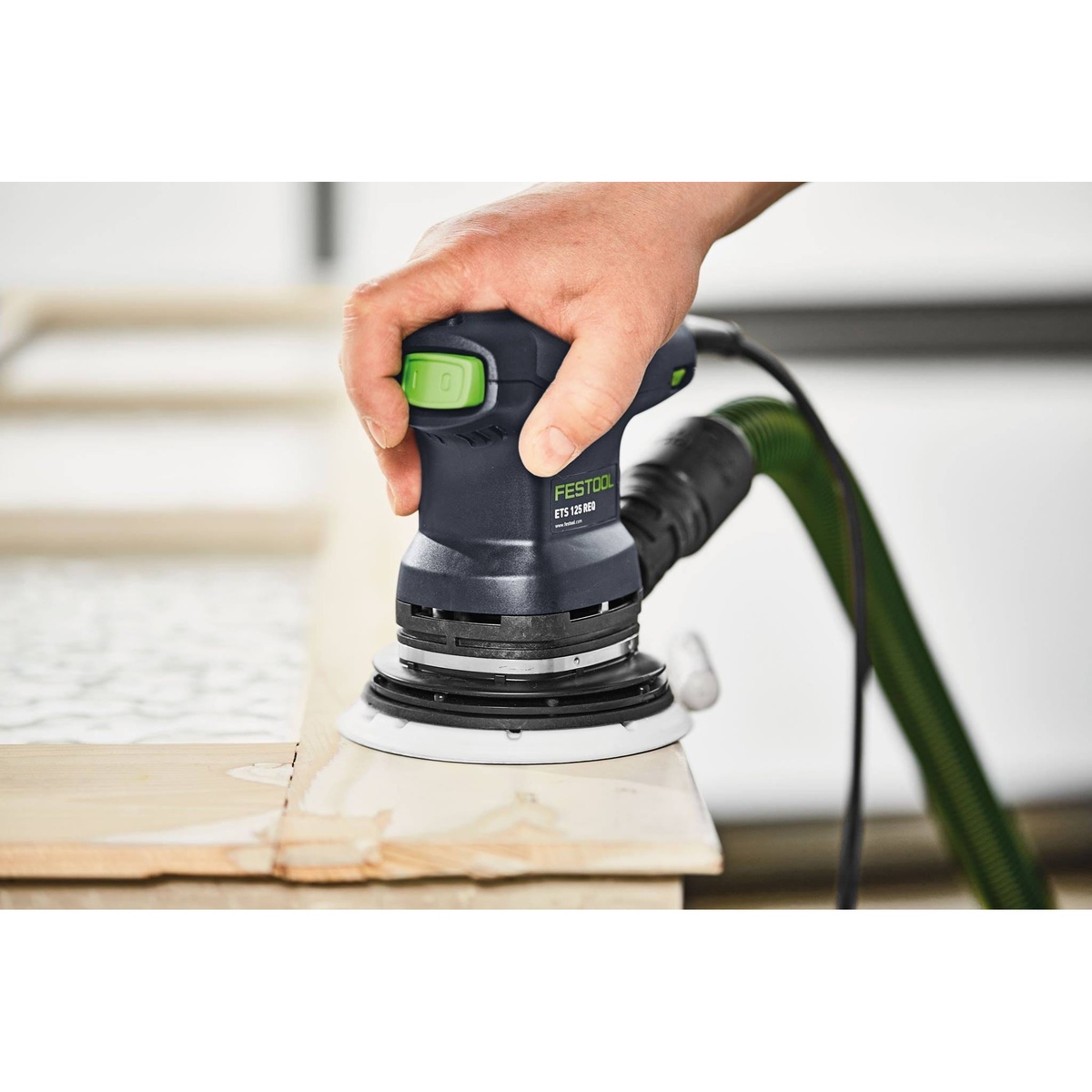 Festool ETS 125 REQ-Plus 125mm random orbital sander smoothing the edge of a wood panel on a bench for finishing work
