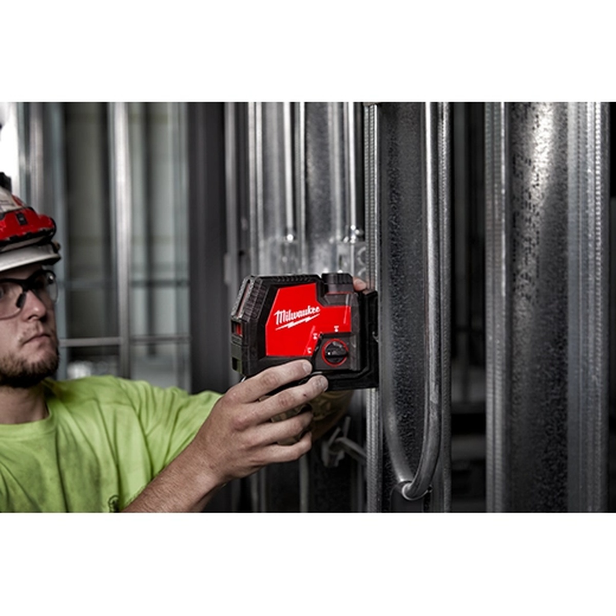 Milwaukee 3521-21 USB Rechargeable Green Cross Line Laser being positioned by a worker on steel framing inside an active construction environment