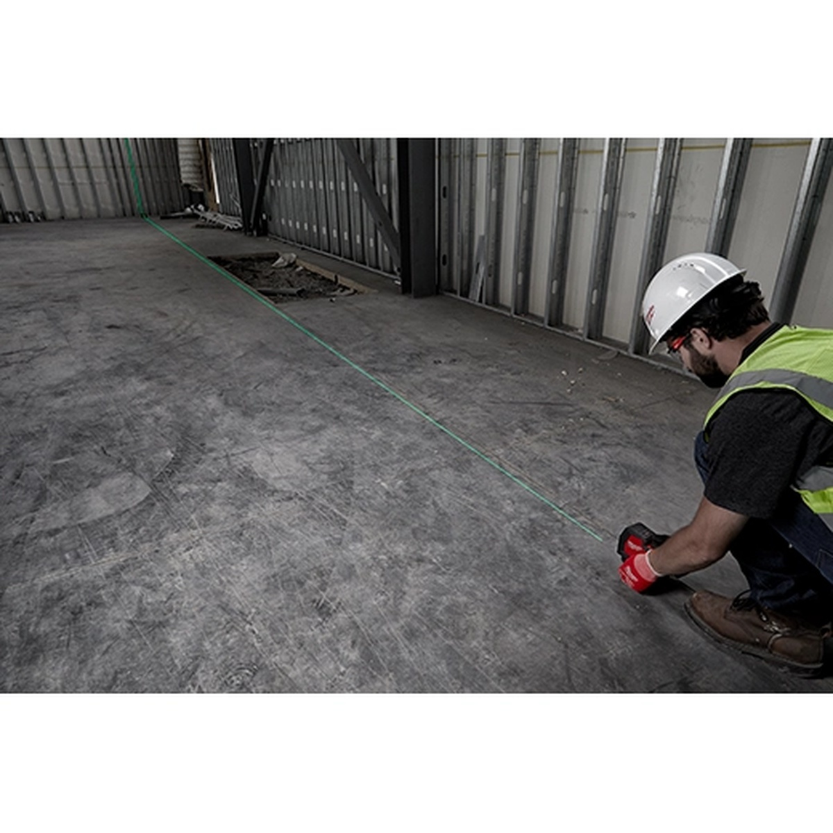 Milwaukee 3521-21 USB Rechargeable Green Cross Line Laser projecting a green horizontal line across a concrete floor during interior layout work on a commercial jobsite