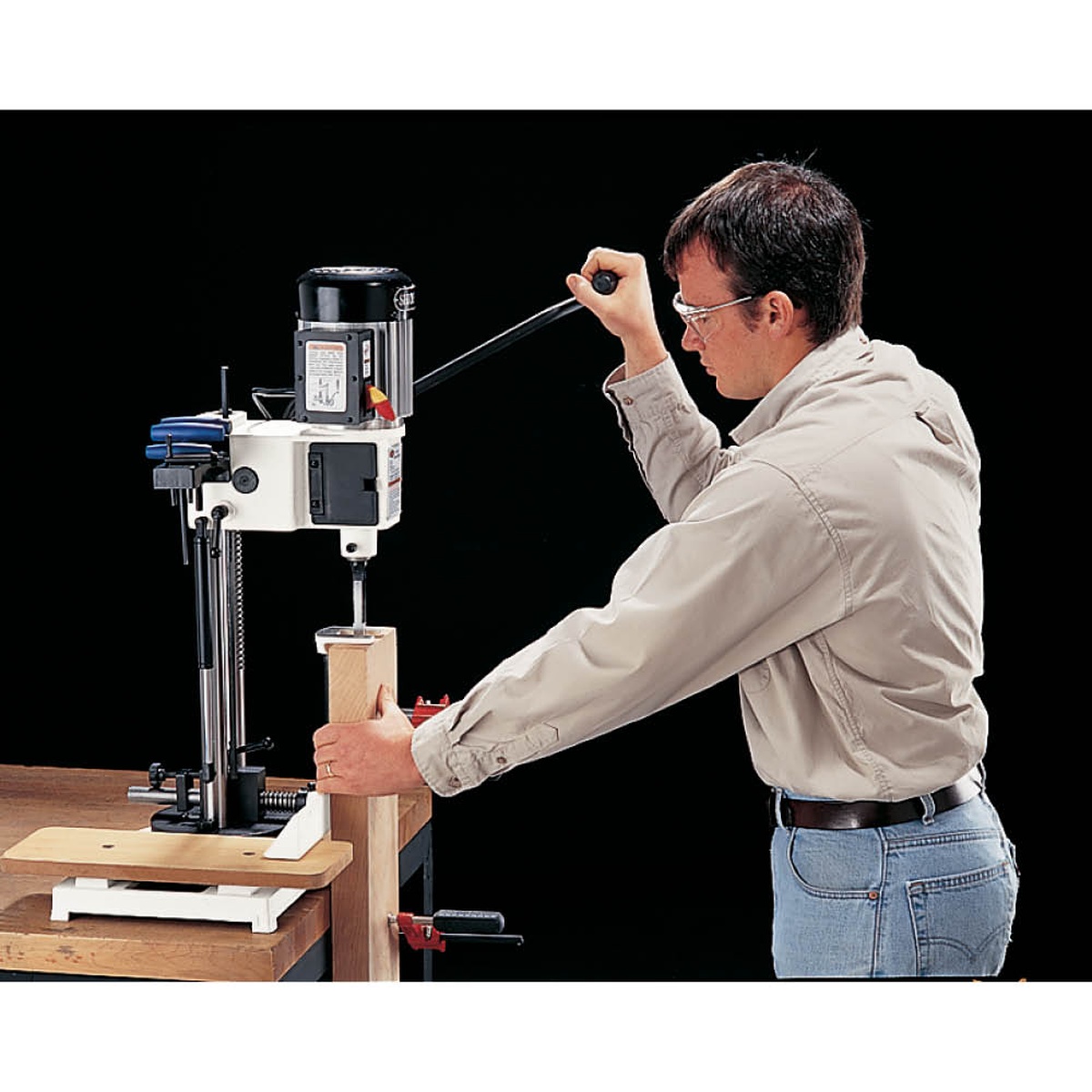Shop Fox W1671 Mortising Machine cutting a mortise into a vertical wood workpiece on a shop bench during woodworking joinery