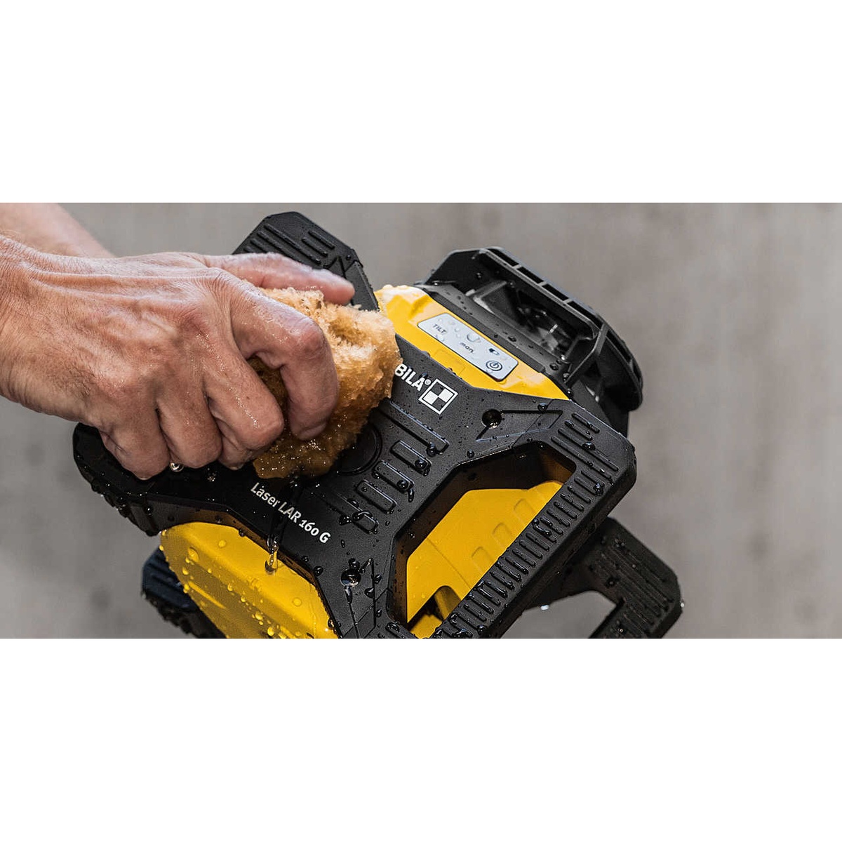Stabila 04500TR LAR 160 G Rotation Laser Set With Tripod and Grade Rod being handled on a wet jobsite to show IP 65 dustproof waterproof protection