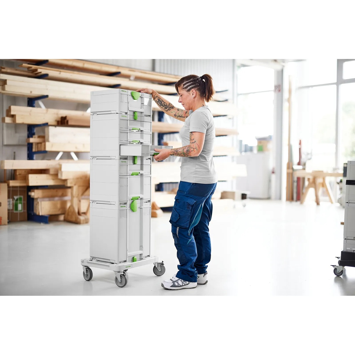 Festool SYS-RB Systainer Roll Board holding a tall stack of Systainer storage cases in a workshop while a user accesses drawers and compartments