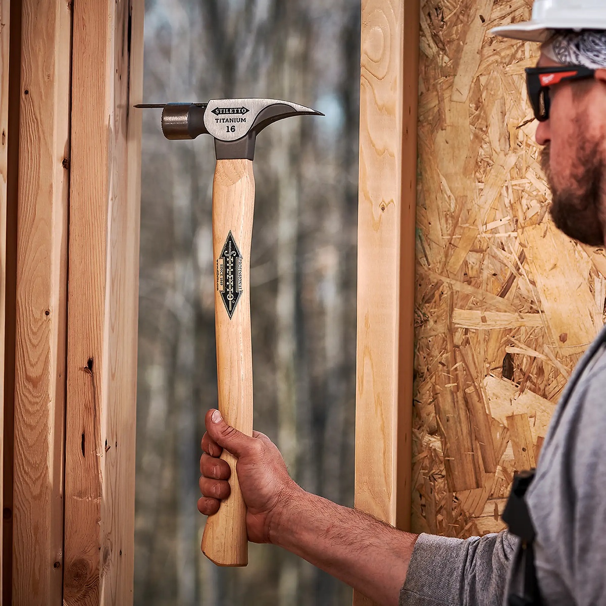 Stiletto TI16MC 16 oz Titanium Milled Face Hammer held on a framing jobsite between wall studs, showing real-world use for rough framing and remodeling