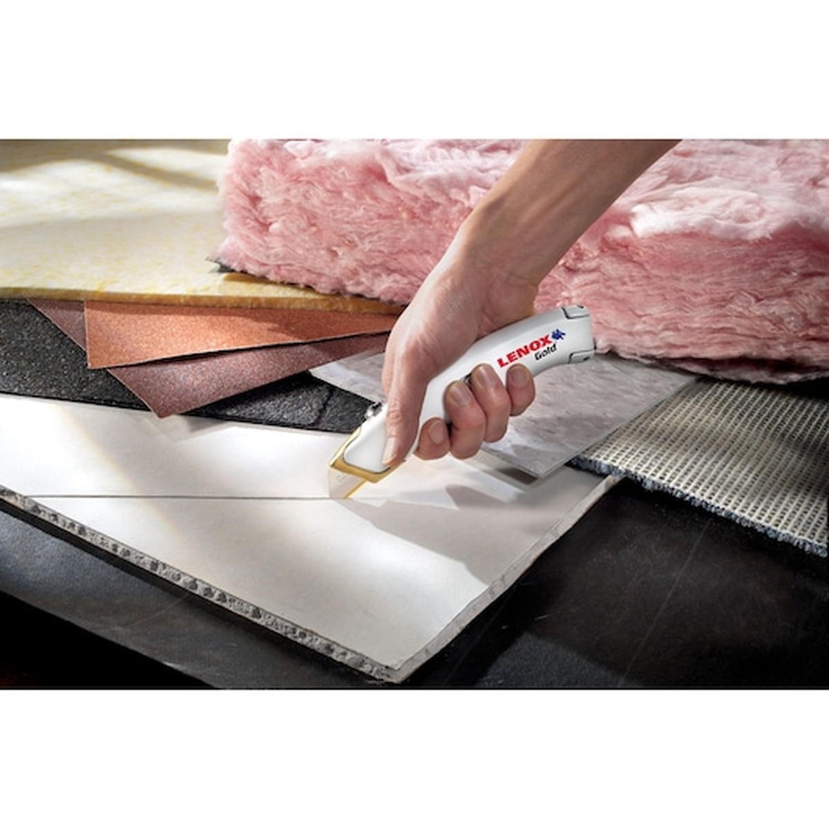 Lenox 20353SSRK1 Gold Quick-Change Retractable Utility Knife cutting sheet material on a work surface beside insulation during remodeling or installation work