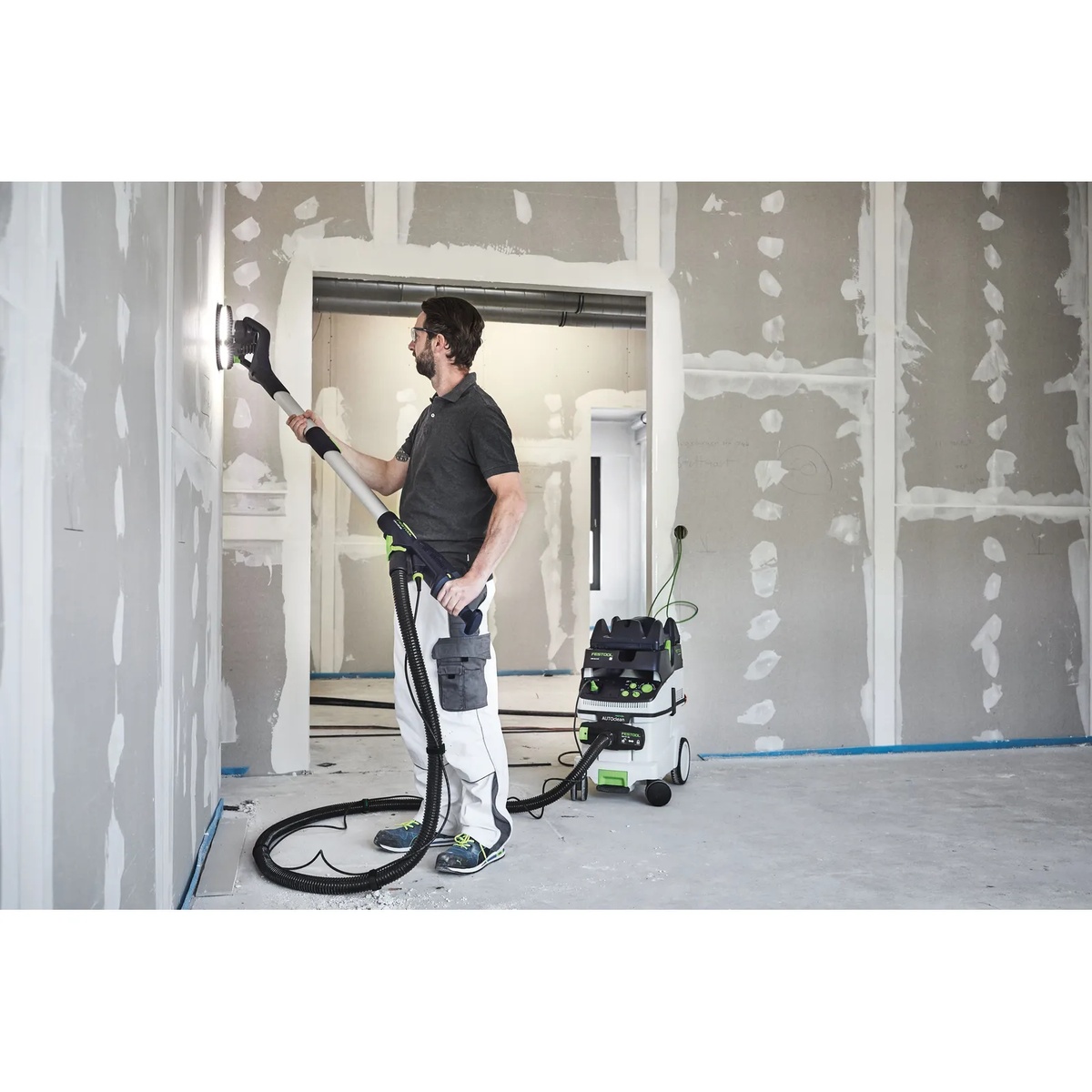 Festool LHS 2 225 EQI-Plus Drywall Sander sanding a finished drywall wall in a room with the LED light ring revealing surface imperfections during interior finishing work