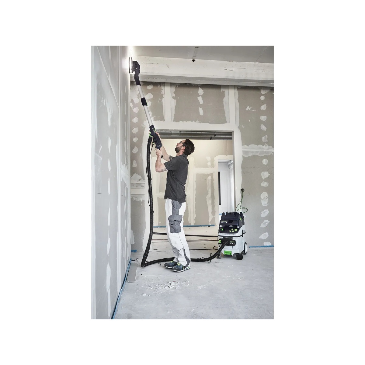 Festool LHS 2 225 EQI-Plus Drywall Sander sanding high drywall near a ceiling with a vacuum connected for overhead finishing on a jobsite