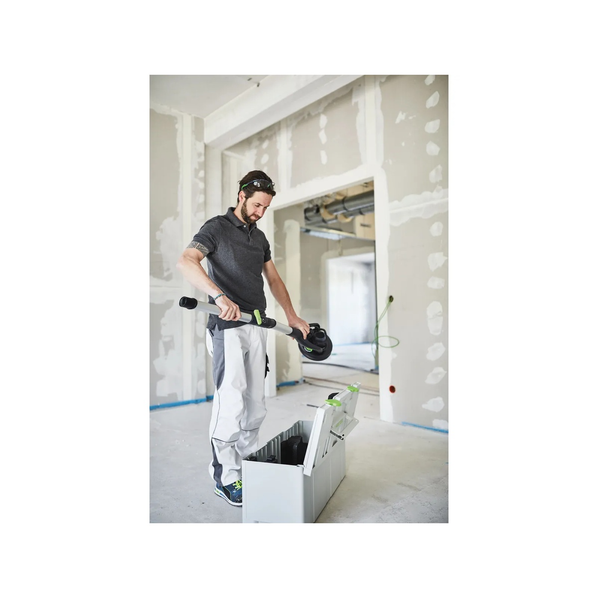Tradesperson lifting a PLANEX long-reach sander with extension from a Systainer in a drywall finishing room before overhead sanding