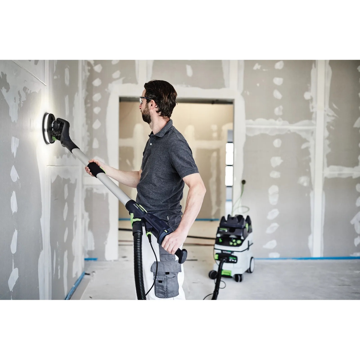 PLANEX drywall sander with Festool extension sanding a finished wall surface inside a remodel space with dust extractor connected