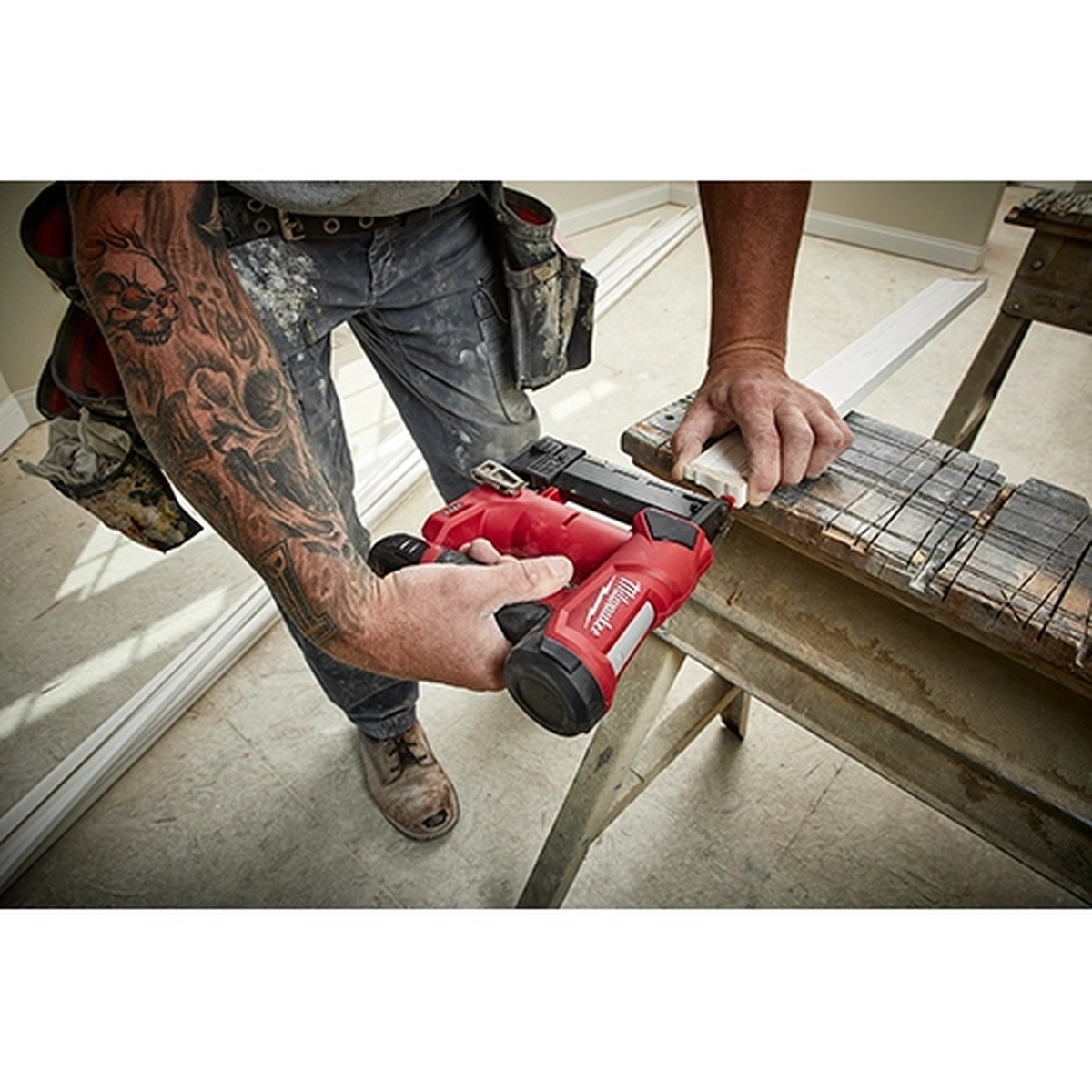 Milwaukee M12 cordless pin nailer being used on trim stock at a workbench during interior finish carpentry