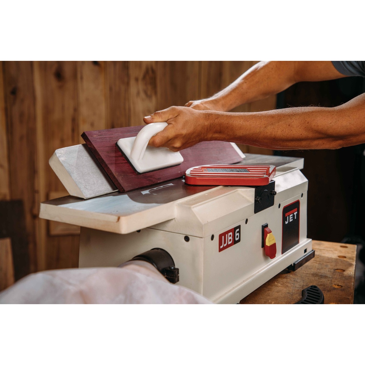 JET 718600 JJ-6HHBT, 6-Inch Helical Head Benchtop Jointer smoothing the edge of a hardwood board on a workbench in a woodworking shop