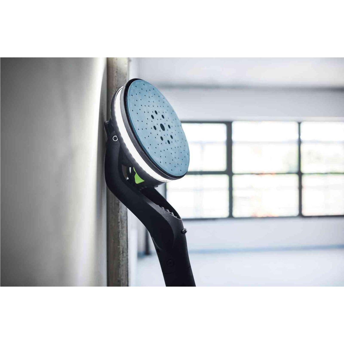 Festool Planex drywall sander head pressed against an interior wall during drywall finishing, showing the large sanding pad and light ring in a clean remodeling environment