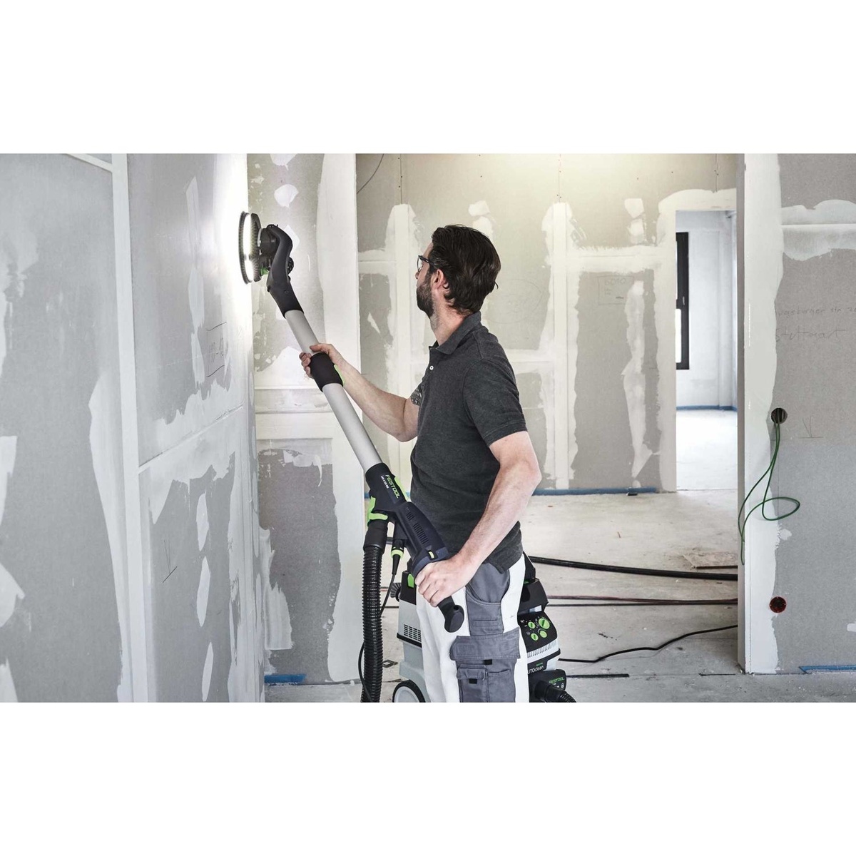Festool 575994 Planex 2.0 Drywall Sander + CT 36 EI AutoClean Dust Extractor Bundle in use sanding finished drywall on an interior wall with the connected dust extractor behind the operator