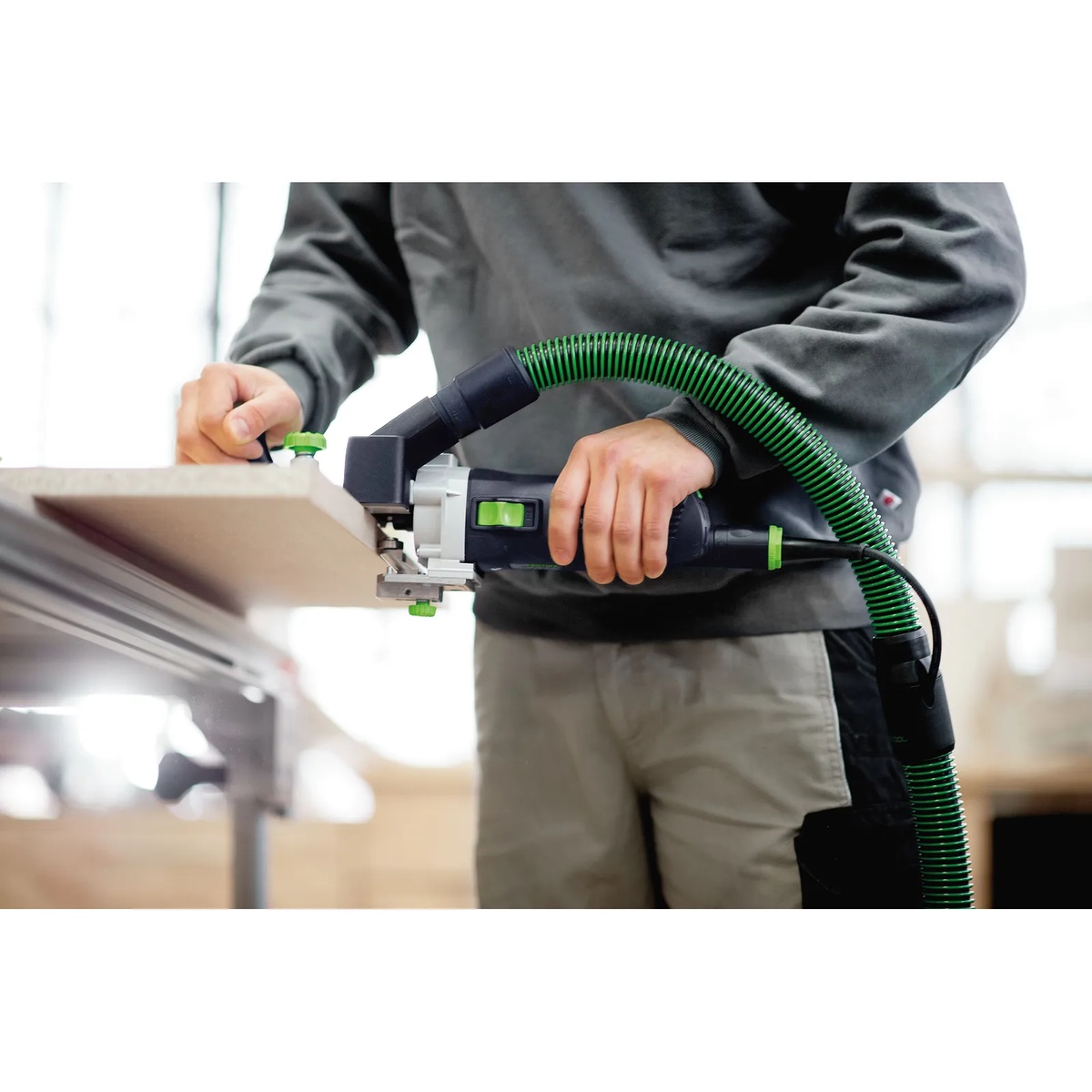 Festool MFK 700 edge router used horizontally on panel edging with vacuum hose connected for dust collection in a cabinet shop