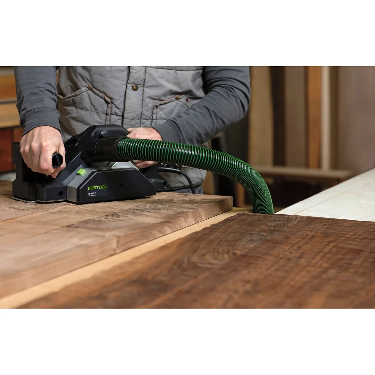 Festool HL 850 E-F-Plus Planer smoothing a wide hardwood panel on a workbench with dust extraction connected in a woodworking shop