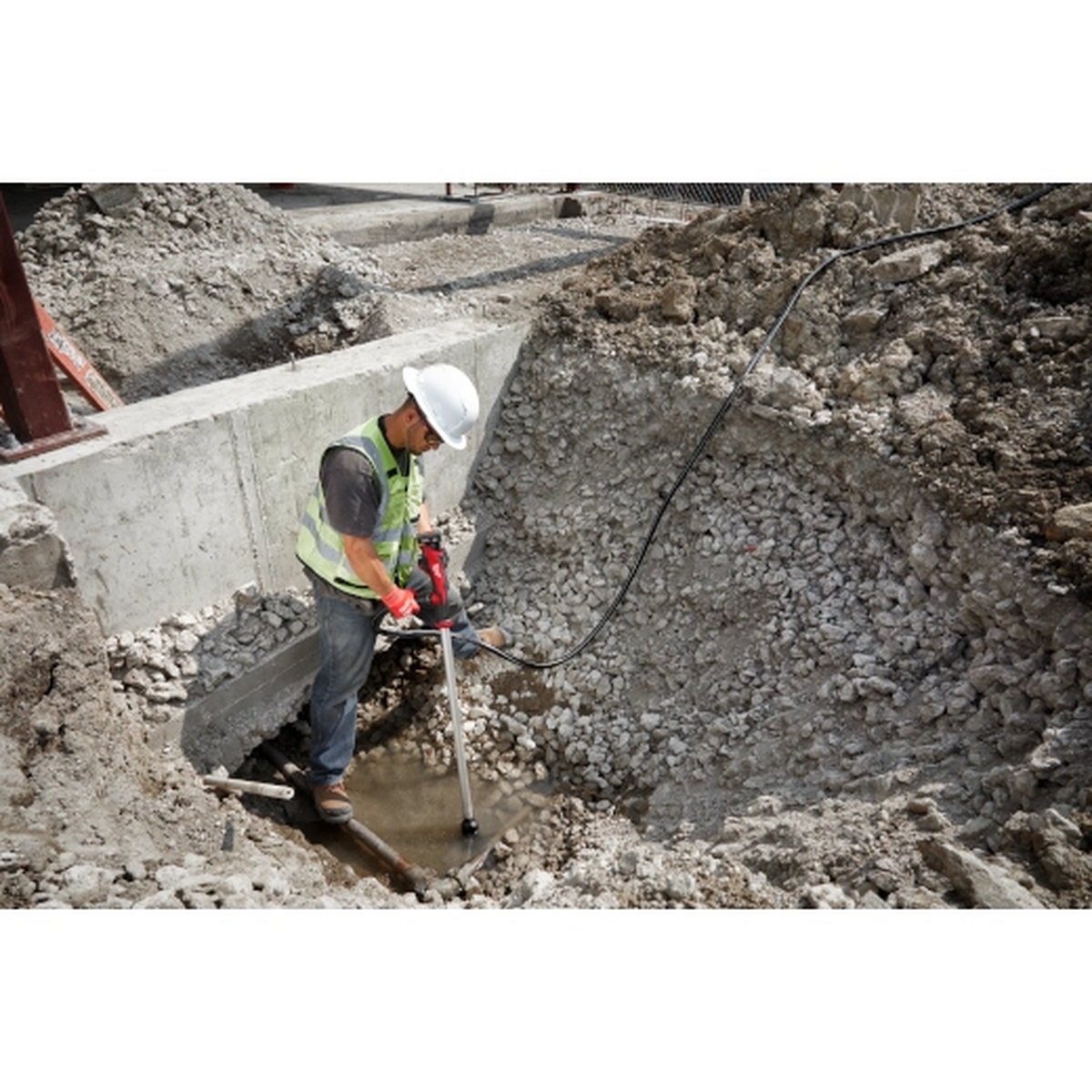 Milwaukee 2579-20 M12 Stick Transfer Pump removing muddy water from a construction trench with debris around the inlet area