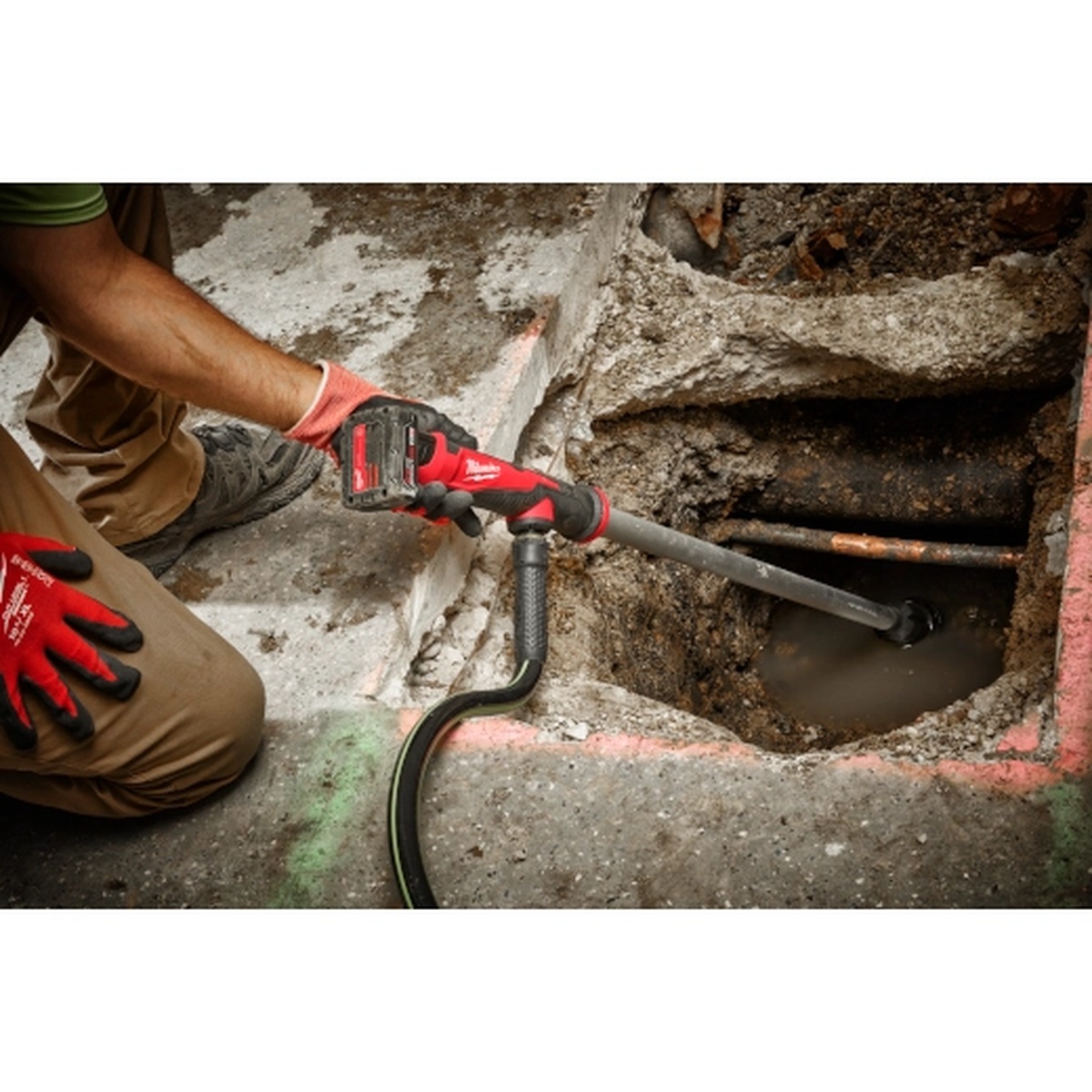 Milwaukee 2579-20 M12 Stick Transfer Pump lowered into a tight utility pit to remove standing water during plumbing or service work