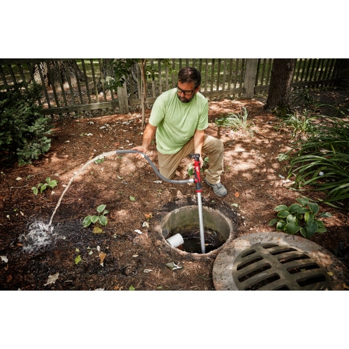 Milwaukee 2579-20 M12 Stick Transfer Pump clearing water from a catch basin using a garden hose discharge in an outdoor drainage repair setting