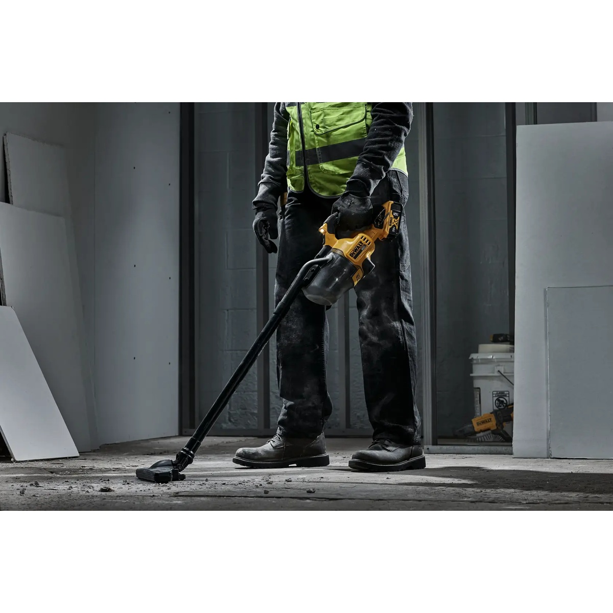 DEWALT DCV501HB 20V MAX Cordless Dry Hand Vacuum cleaning drywall dust and debris from a concrete floor on an indoor jobsite with extension tube and floor nozzle