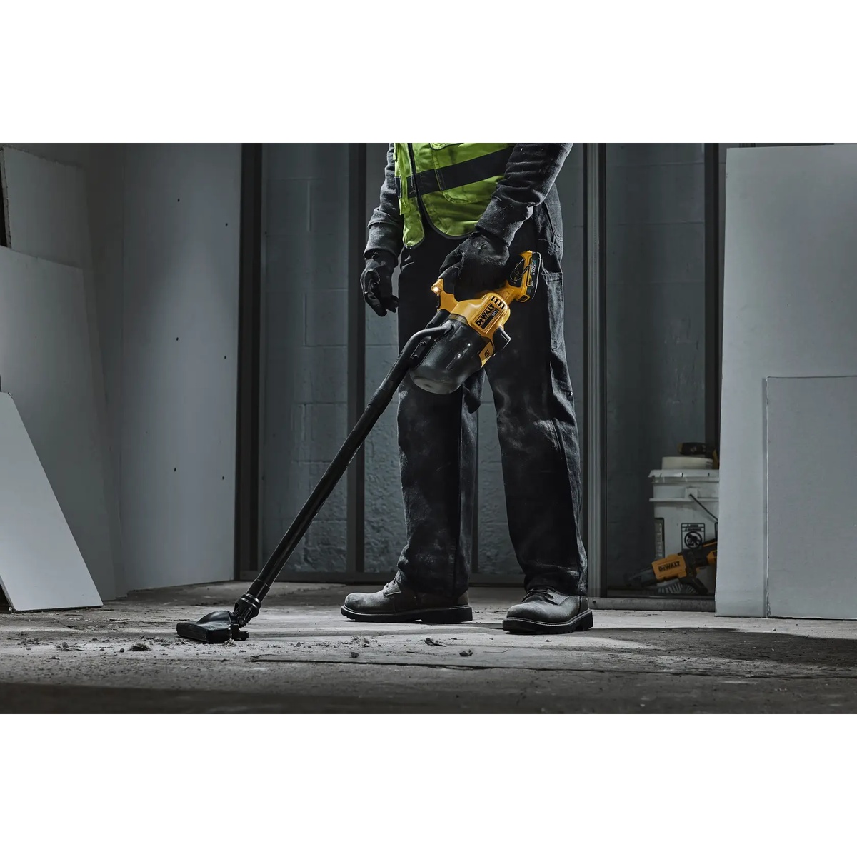 DEWALT DCV501HB cordless handheld vacuum in use on a construction site picking up dry debris near wall edges with the extension tube attached