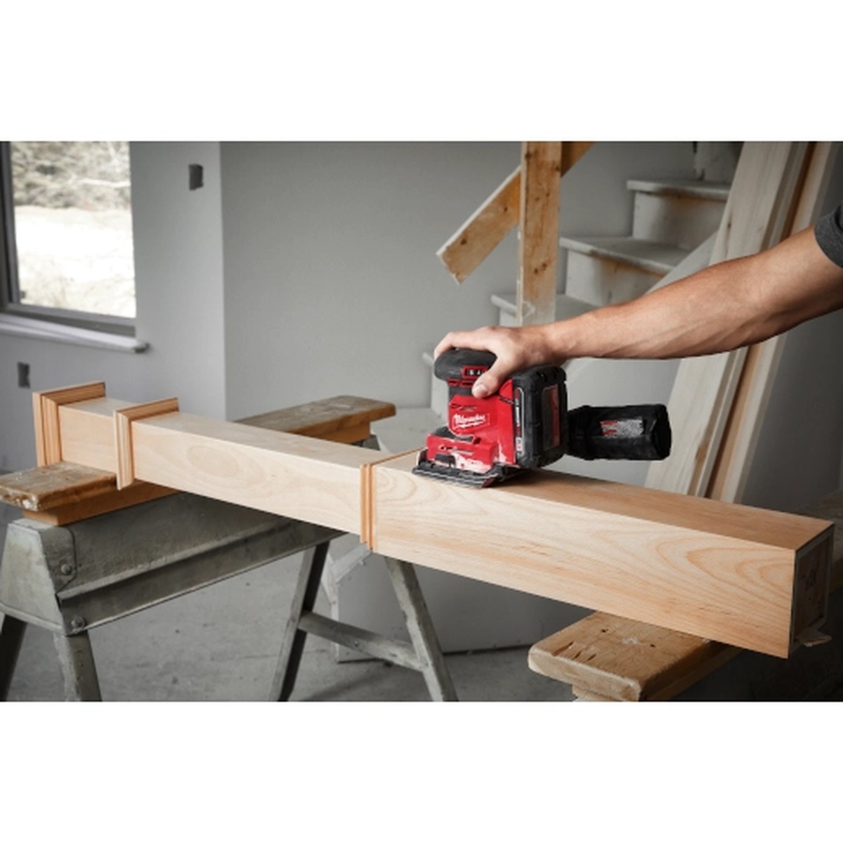 Milwaukee 2649-20 M18 Orbital 1/4 Sheet Sander sanding a wood beam indoors during trim and finish work
