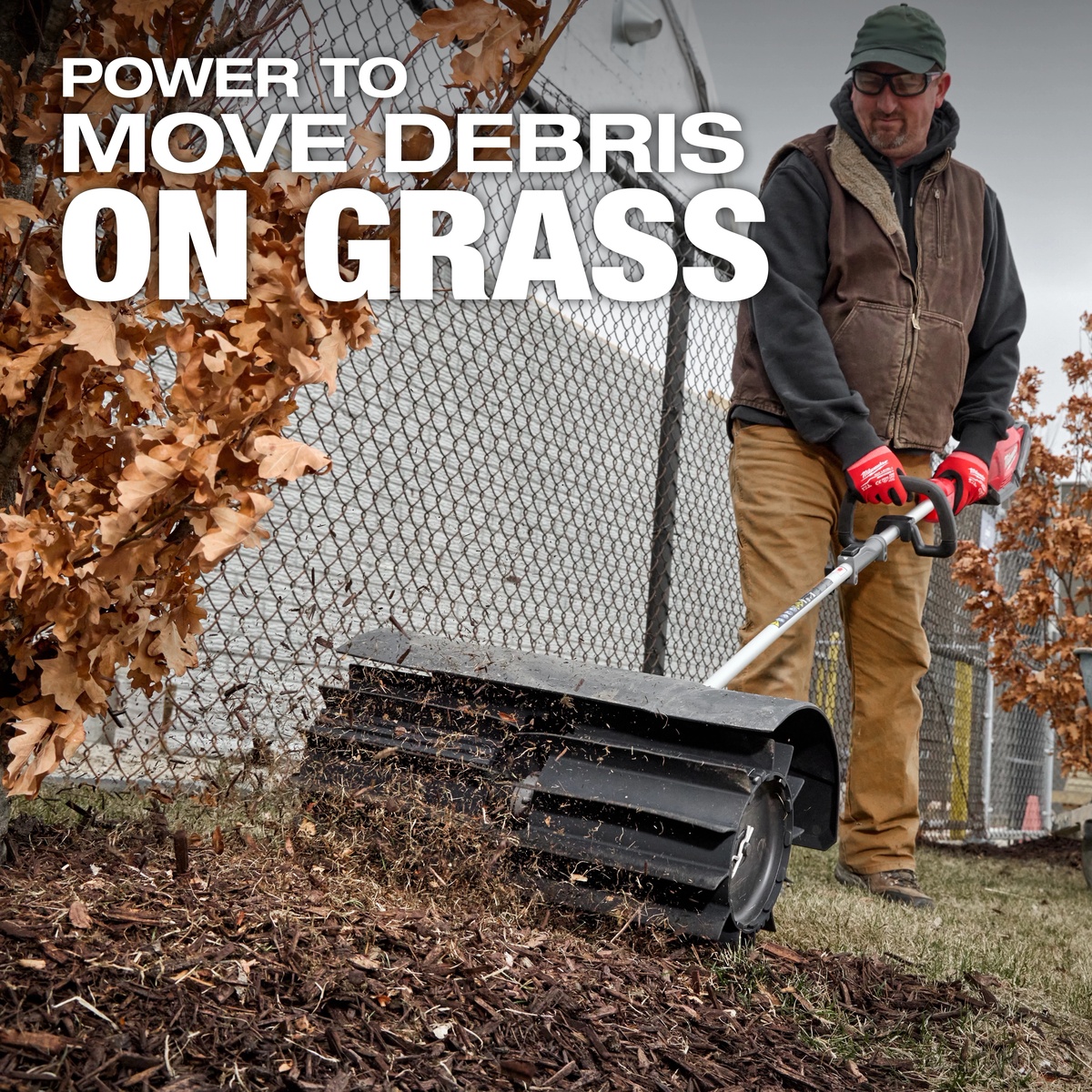 Milwaukee 49-16-2740 M18 FUEL QUIK-LOK Rubber Broom Attachment moving mulch and loose debris across grass along a fence line during outdoor cleanup