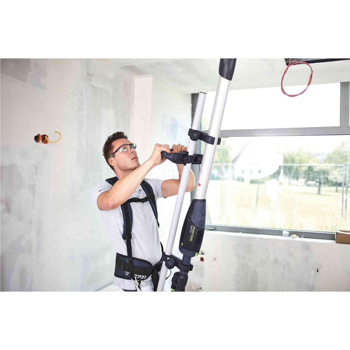 Festool 576802 PLANEX Drywall Sander Harness TG-LHS 225 w/ Systainer3 with operator adjusting the support handle on a PLANEX sander inside a drywall finishing jobsite