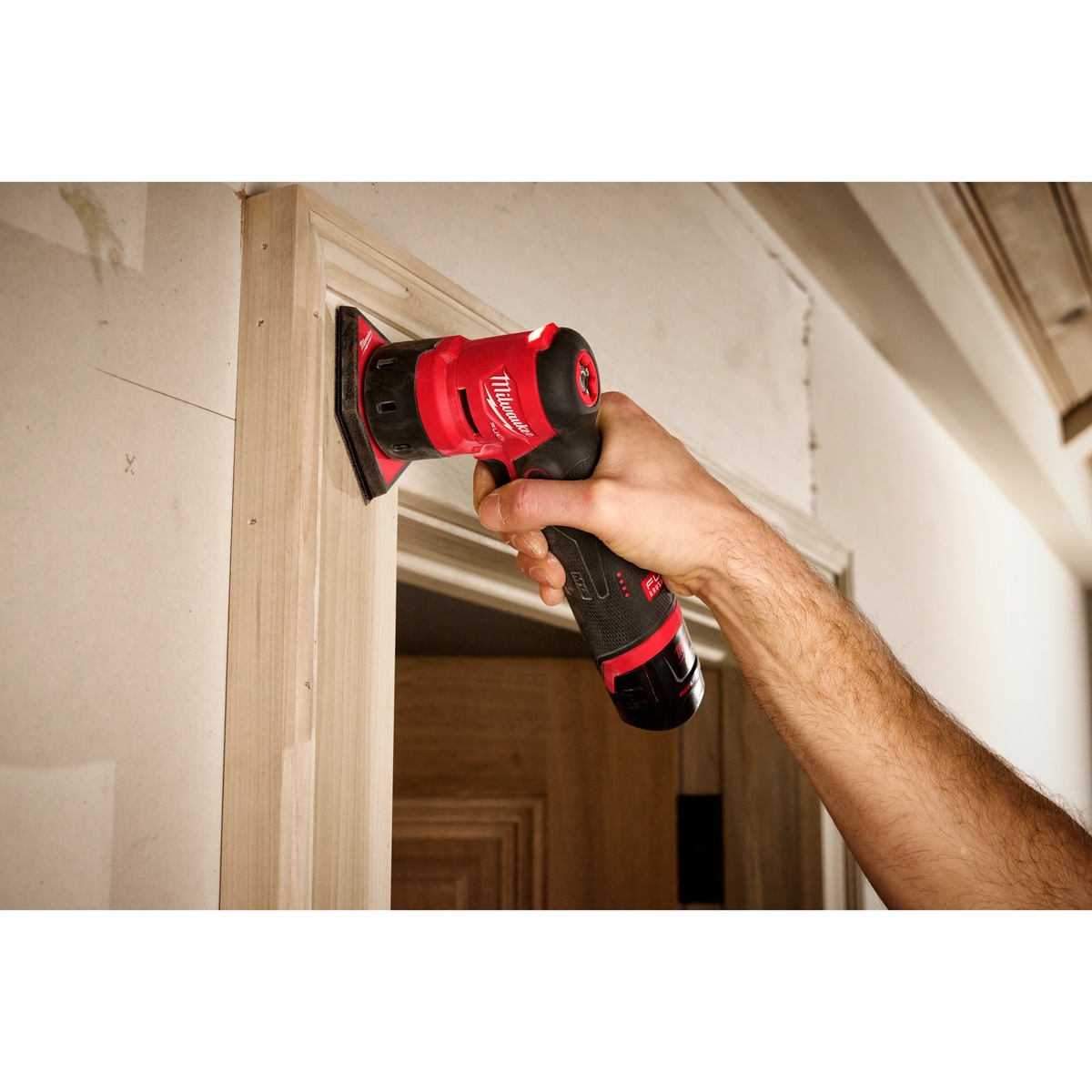 Milwaukee 2531-20 M12 FUEL Orbital Detail Sander sanding interior door trim in place during finish carpentry work