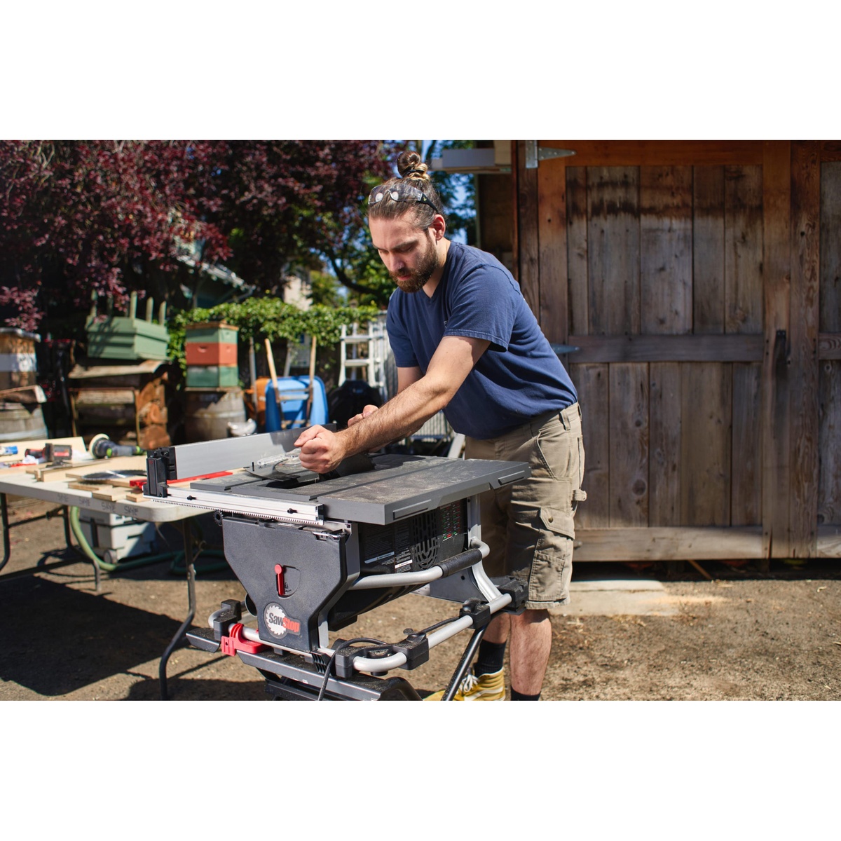 SawStop CTS-120A60 10 inch Compact Table Saw set up on a stand outdoors at a jobsite while a user adjusts the fence for wood cutting