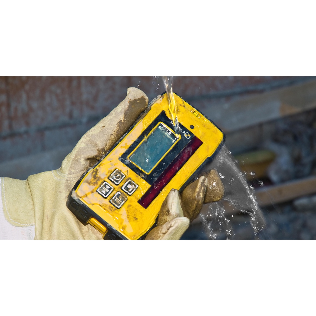 Stabila REC 300 Digital Receiver being rinsed with water while held in work gloves on a muddy jobsite